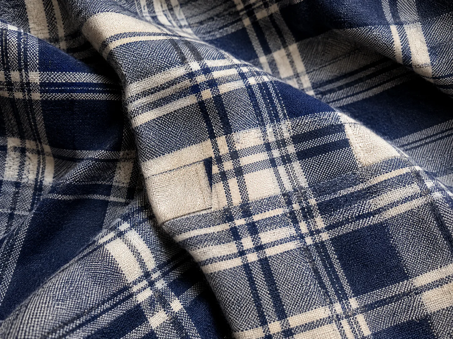 Edited result: Synthetic plaid fabric with a size label crossing the checked pattern, before and after one text-removal edit