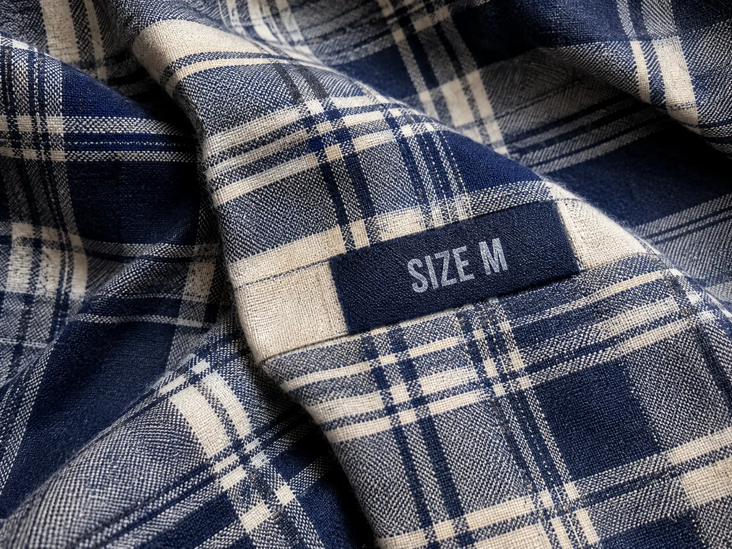 Synthetic input: Synthetic plaid fabric with a size label crossing the checked pattern, before and after one text-removal edit